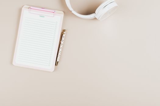 A simplistic flat lay of a notepad, pen, and headphones on a white background.