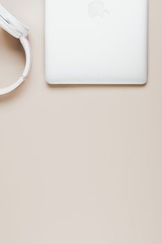 Simple flat lay photo of laptop and headphones on beige background, offering ample copy space.