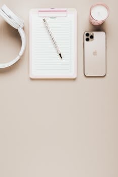 Elegant minimalist workspace featuring a smartphone, notepad, pen, and headphones on a beige background.
