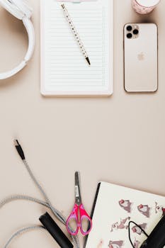 Top view of a creative workspace featuring a smartphone, headphones, notebook, and stationery.