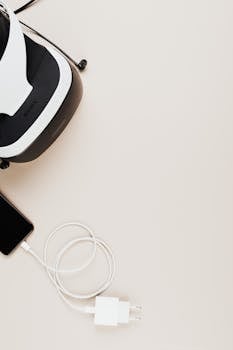 VR headset and smartphone with a charger on a light background, offering copy space.