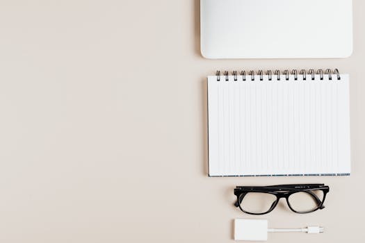 最小办公桌设置的顶视图，展示着记事本、笔记本电脑、眼镜和适配器