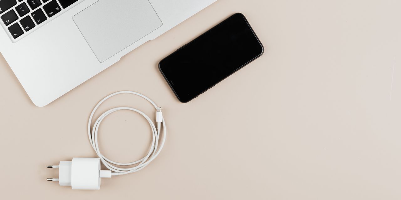 Flat lay of a laptop, smartphone, and charger on a beige background showcasing modern technology essentials.