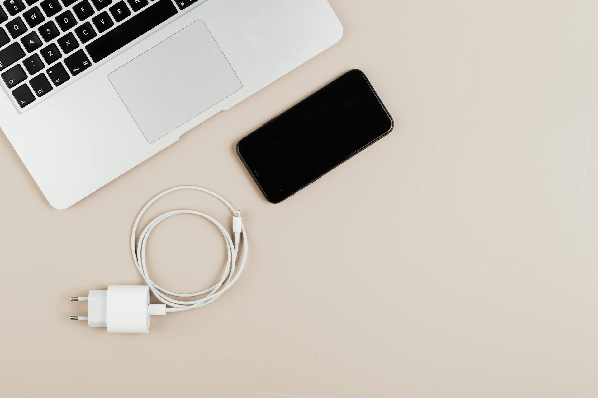 Flat lay of a laptop, smartphone, and charger on a beige background showcasing modern technology essentials.