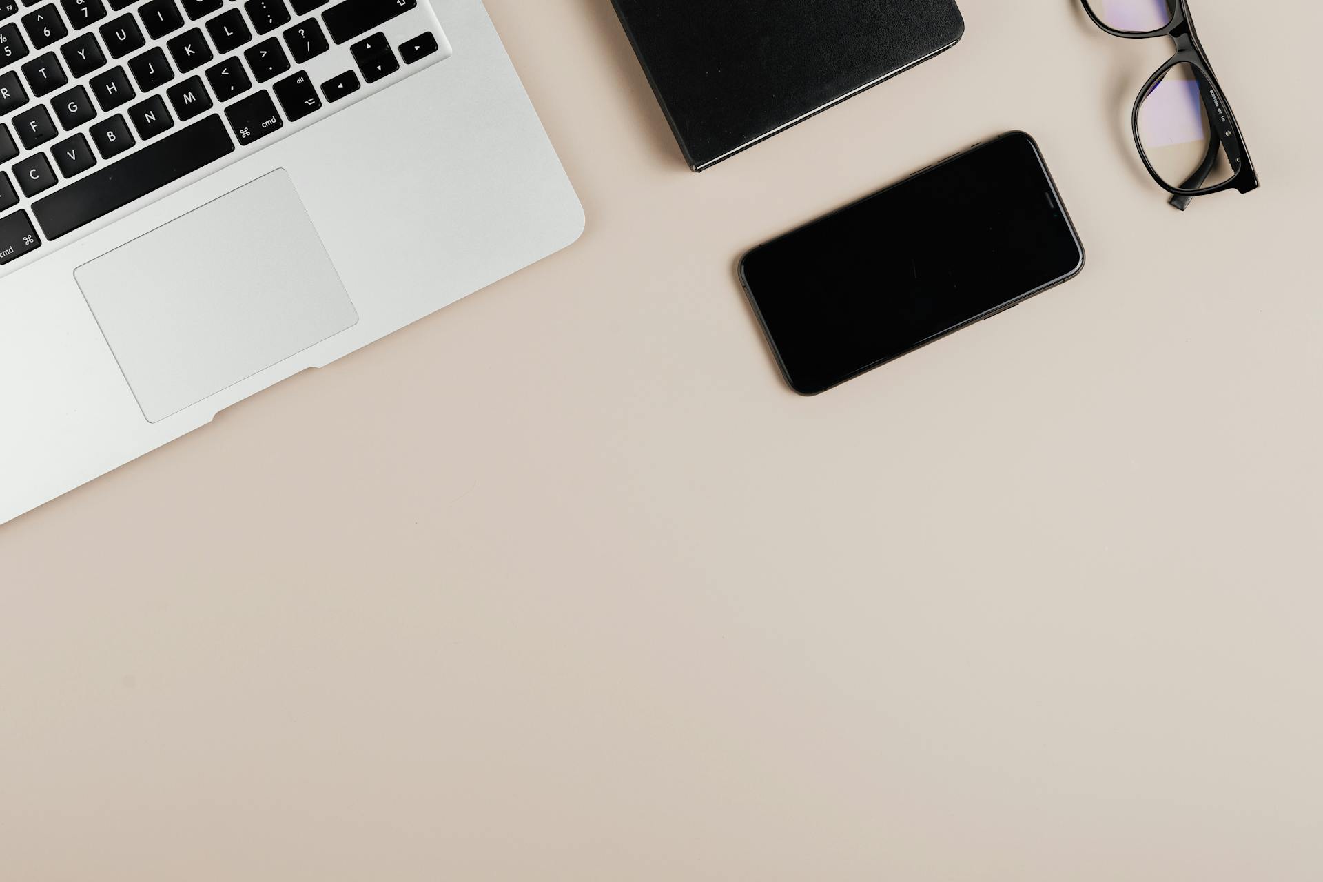 Modern workspace with laptop, smartphone, and eyeglasses on a beige surface. Ideal for tech or productivity themes.