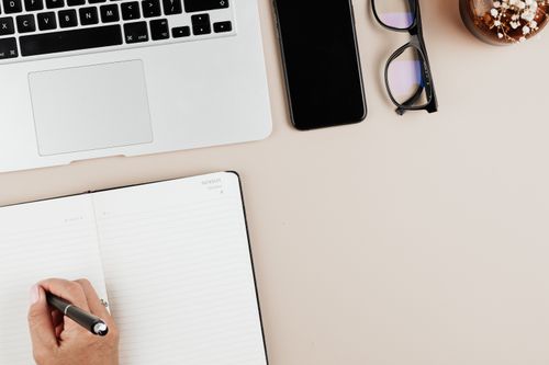 Free Top view of a modern workspace with a laptop, notebook, smartphone, and eyeglasses on a light surface. Stock Photo
