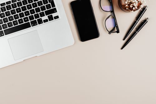 Free Stylish flat lay of a workspace with laptop, smartphone, glasses, and pens on a beige surface. Stock Photo