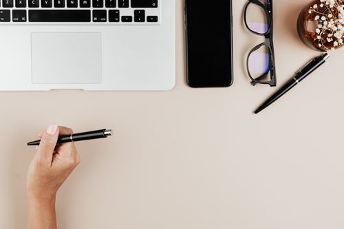 Free Overhead view of a minimalist workspace with a laptop, smartphone, pen, and eyeglasses on a beige surface. Stock Photo