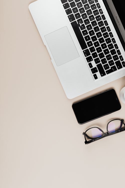 Free Overhead view of a sleek workspace featuring a laptop, smartphone, and eyeglasses on a neutral surface. Stock Photo