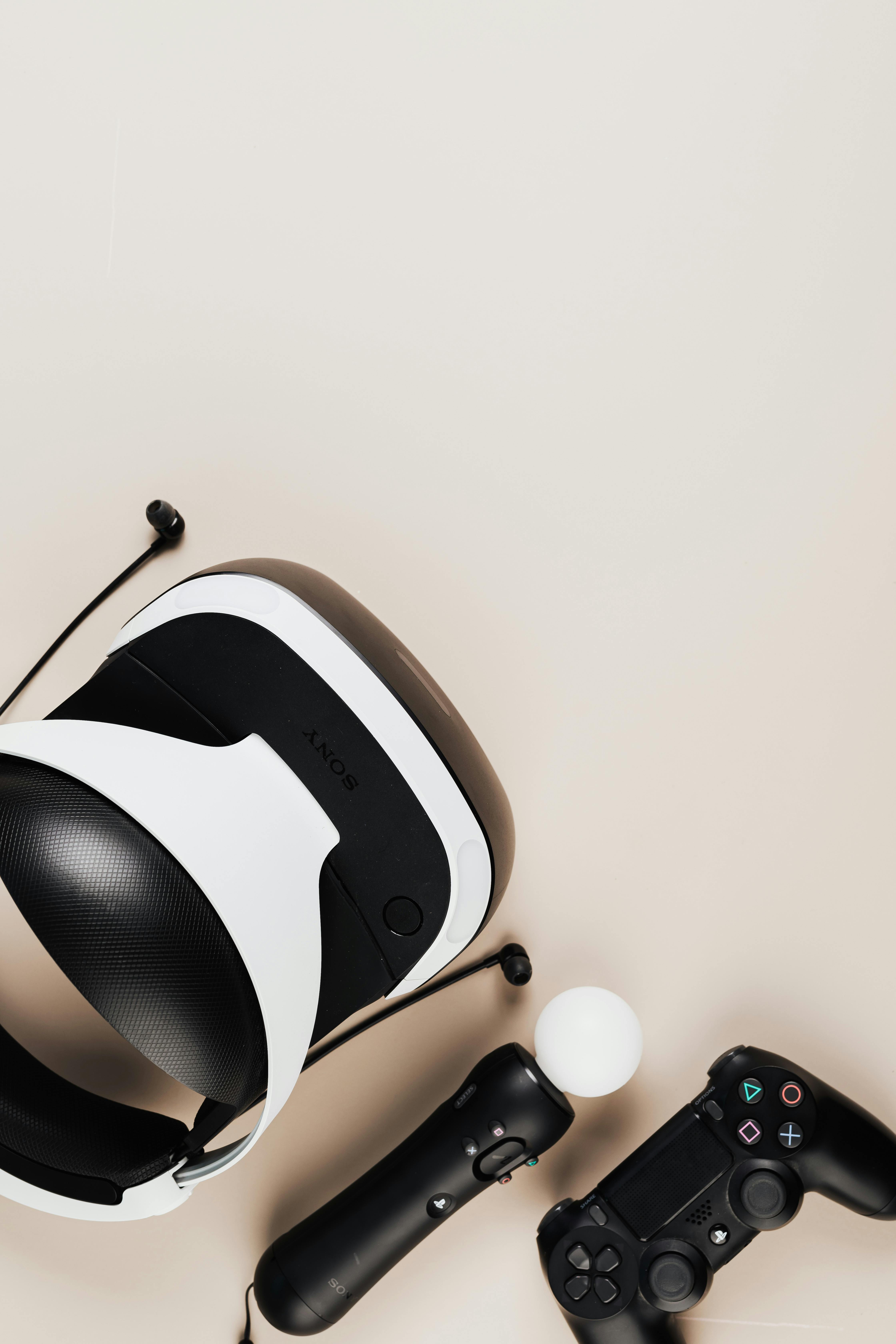 Top view of a virtual reality headset and gaming controllers on a neutral background.