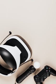 Top view of a virtual reality headset and gaming controllers on a neutral background.
