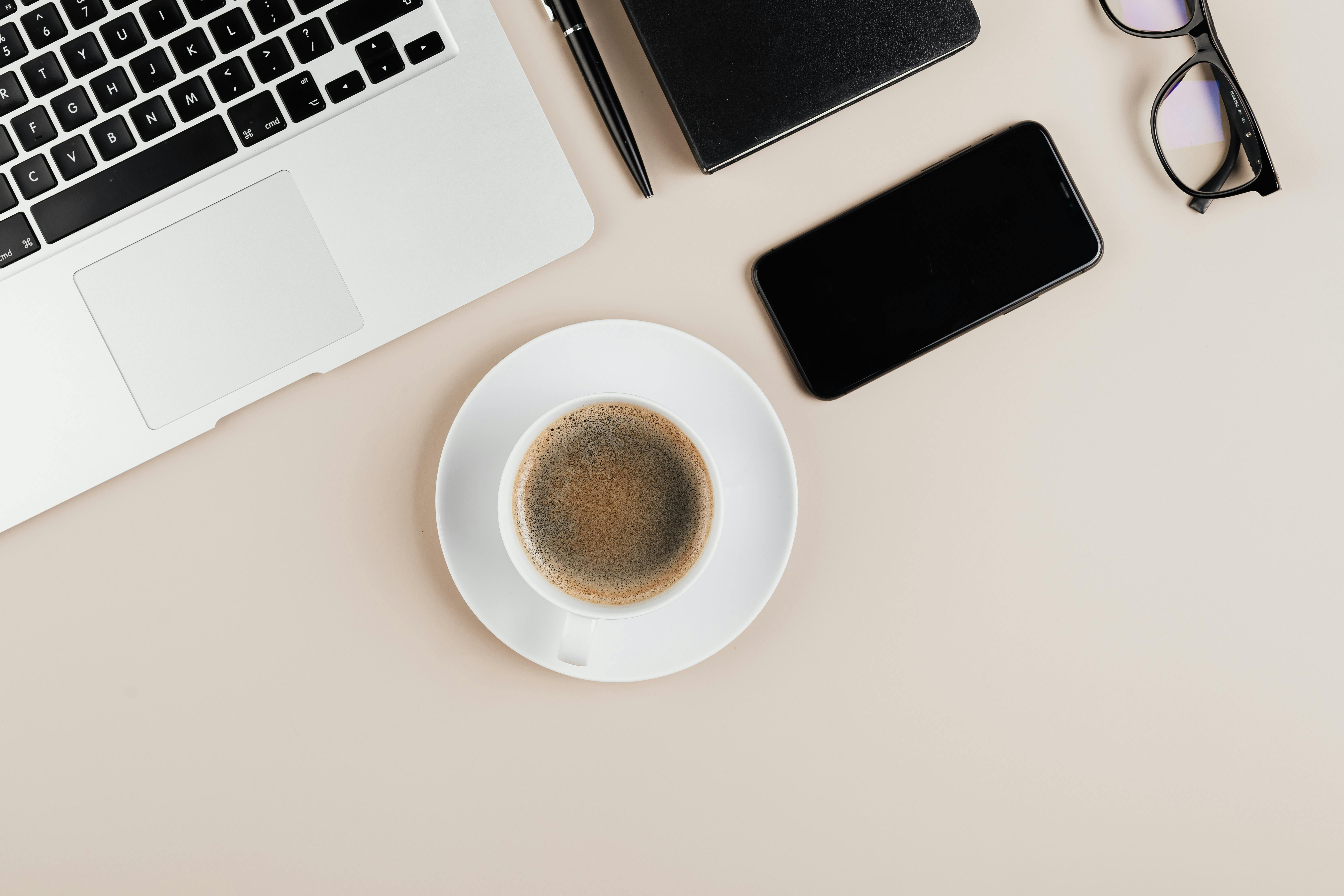现代工作区里，白色背景上摆放着咖啡、笔记本电脑和小工具