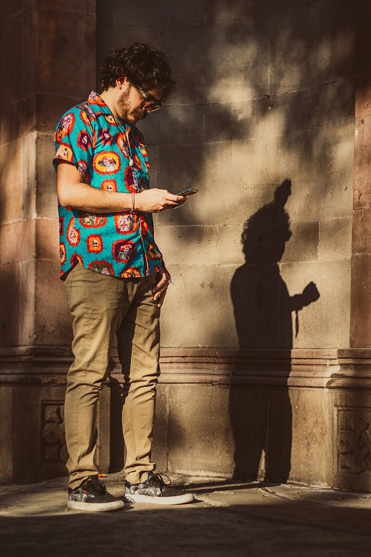 Man In A Colorful Printed Top And Khaki Pants Holding A Smartphone