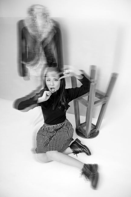 Stereoscopic black and white of Asian female sitting on floor in studio with inverted chair and mannequin with hands near face and looking at camera