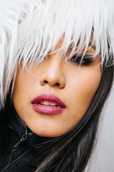 Young Asian female with bright makeup and dark hair with white feathers covering eyes looking at camera in studio inside