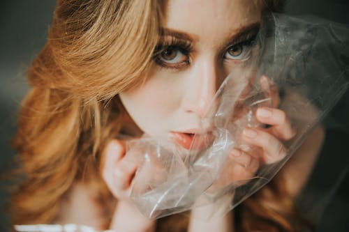 Free From above of young female with blond hair looking at camera with transparent polythene package near face in light room Stock Photo