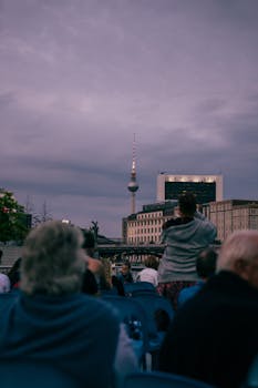 Tourists in Berlin admire the Fernsehturm amidst the cityscape at dusk.