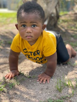 一个穿着黄色衬衫的可爱男婴，正在户外草地上爬行，画面由自然光捕捉