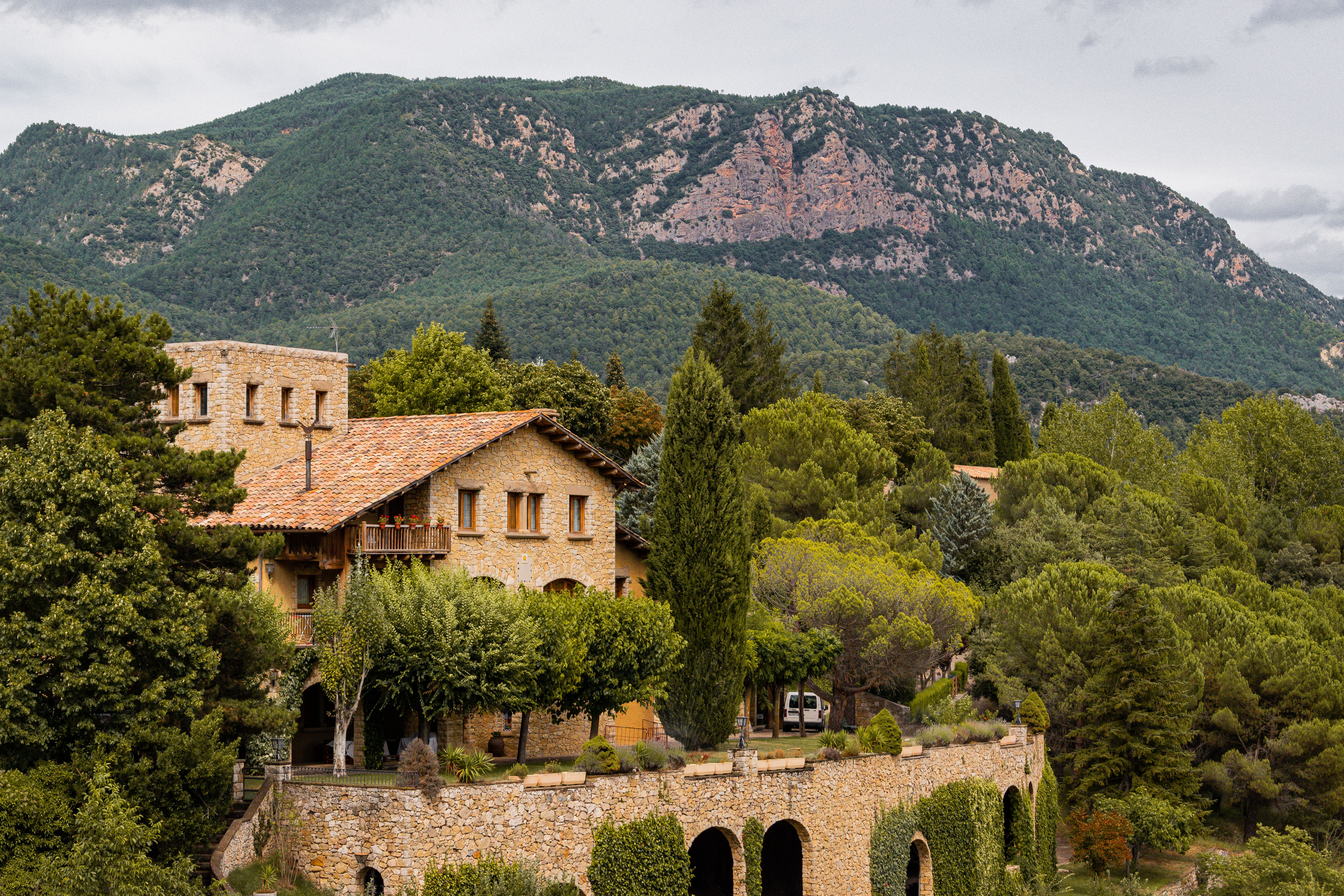 Charming stone house in Solsona surrounded by vibrant greenery and towering mountains.
