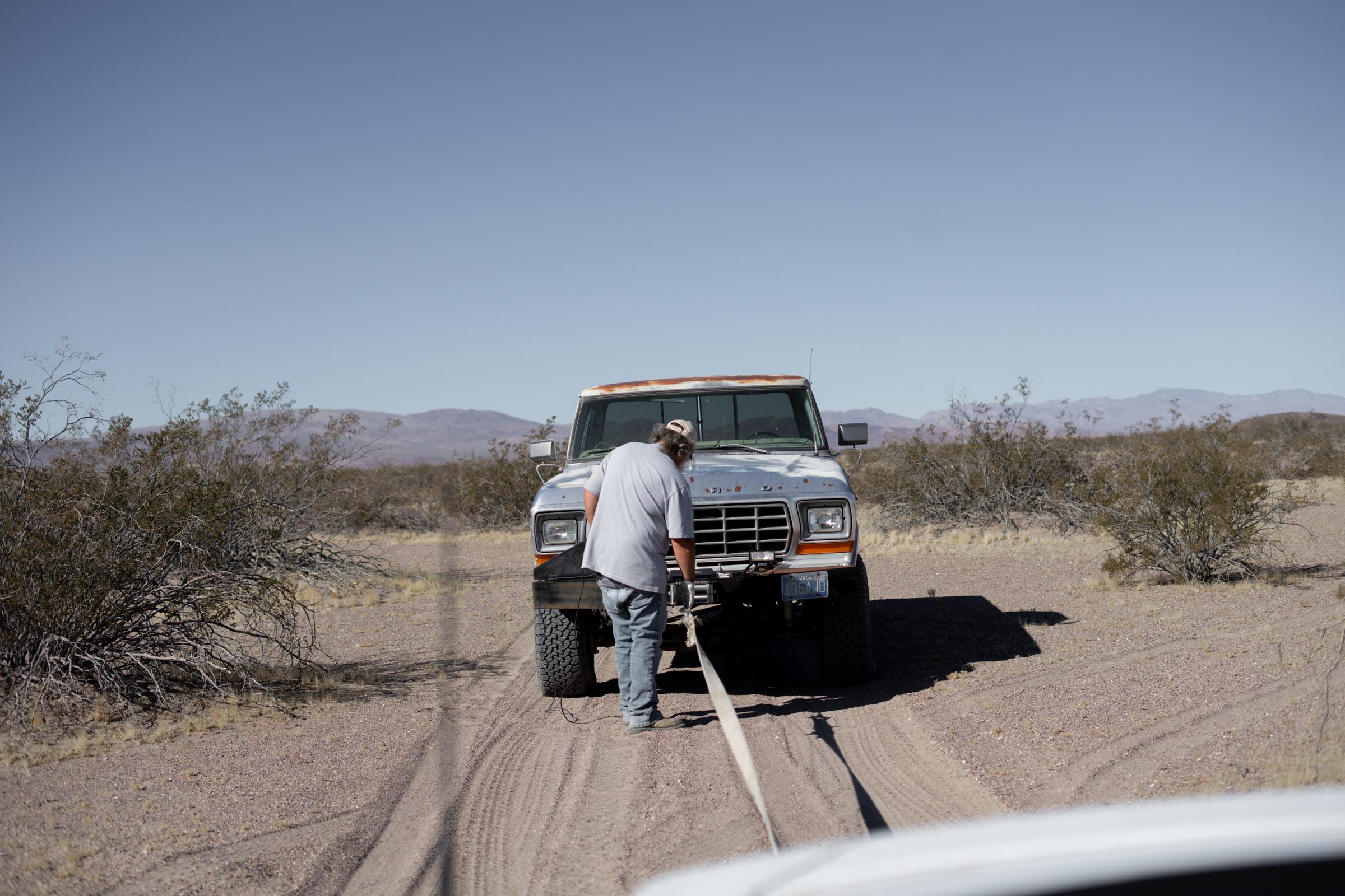 Off-road recovery in progress — driver hooking up a recovery strap to a stuck pickup truck in desert sand