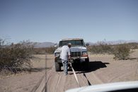 Man Towing a Pick Up Truck on Desert Road