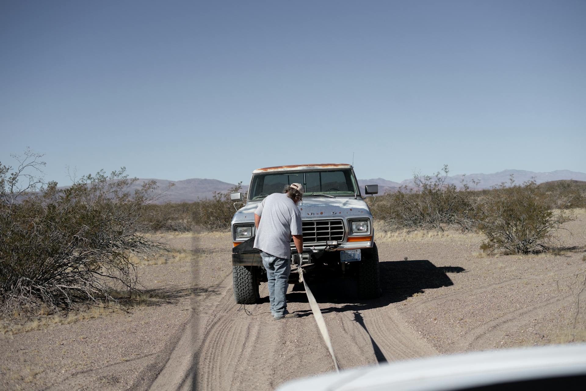 Man Towing a Pick Up Truck on Desert Road