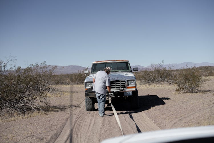 Man Towing A Pick Up Truck On Desert Road