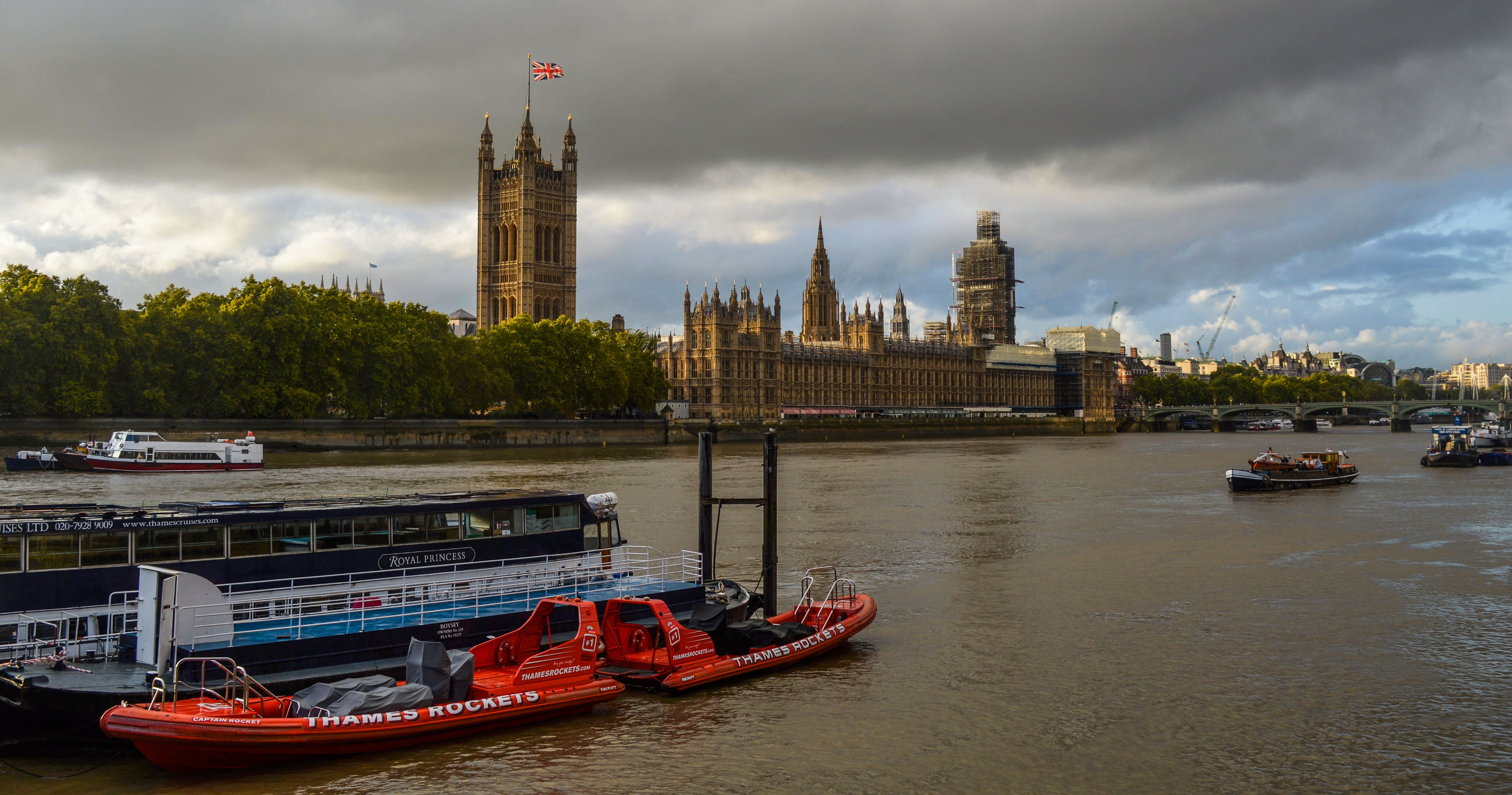 Touristic boats floating on Thames against Houses of Parliament under cloudy sky at daytime