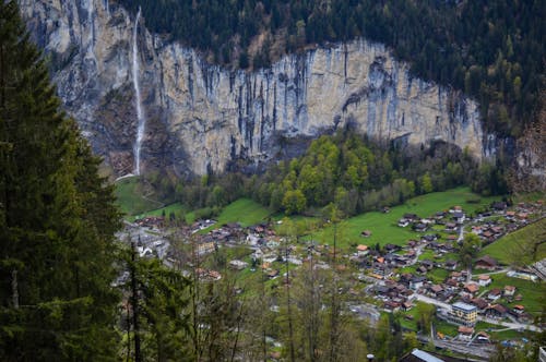 From above of picturesque rocky mountain covered with coniferous trees with waterfall flowing above small village of Lauterbrunnen in Switzerland