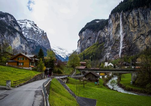 Asphalt walkway near wild river in scenic countryside with small chalets amidst powerful snowy rocky mountains in Lauterbrunnen valley