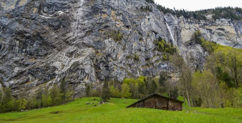Free Old wooden shack on green meadow near massive mountain Stock Photo