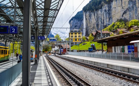 Railways near platforms and high mounts with trees under cloudy sky in daylight