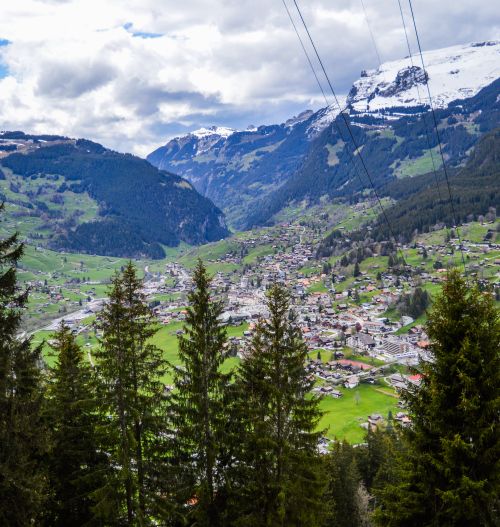 Free From above of village on green hill between high mounts and coniferous trees under shiny cloudy sky Stock Photo