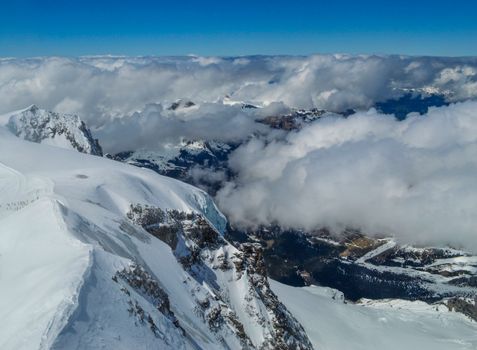 From above top of snowy mountain cliff and majestic clouds over mountainous valley at daytime