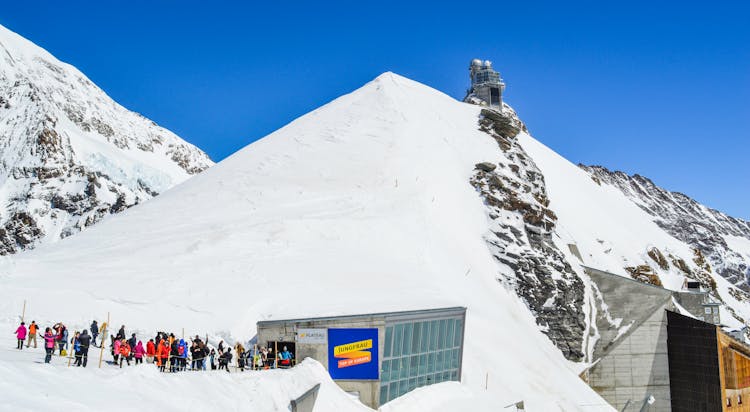 Faceless Travelers In Queue In Snowy Mounts Near House