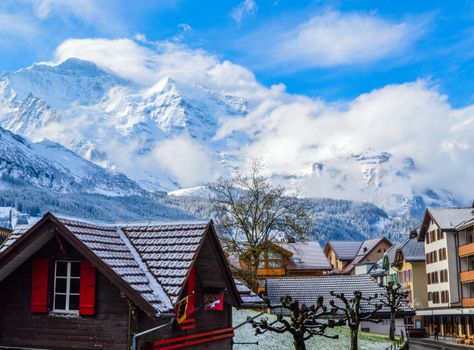 Village with modern cottages placed near high rocky mountains covered with snow in sunny day
