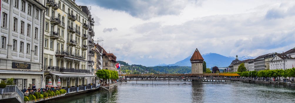 Panoramic view of Chapel Bridge over Reuss River in Lucerne with Swiss Alps in background.
