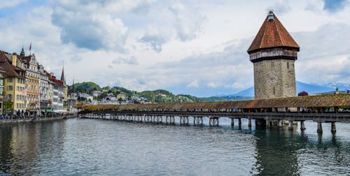 Exterior of medieval Chapel Bridge crossing rippling river in town of Lucerne in cloudy day