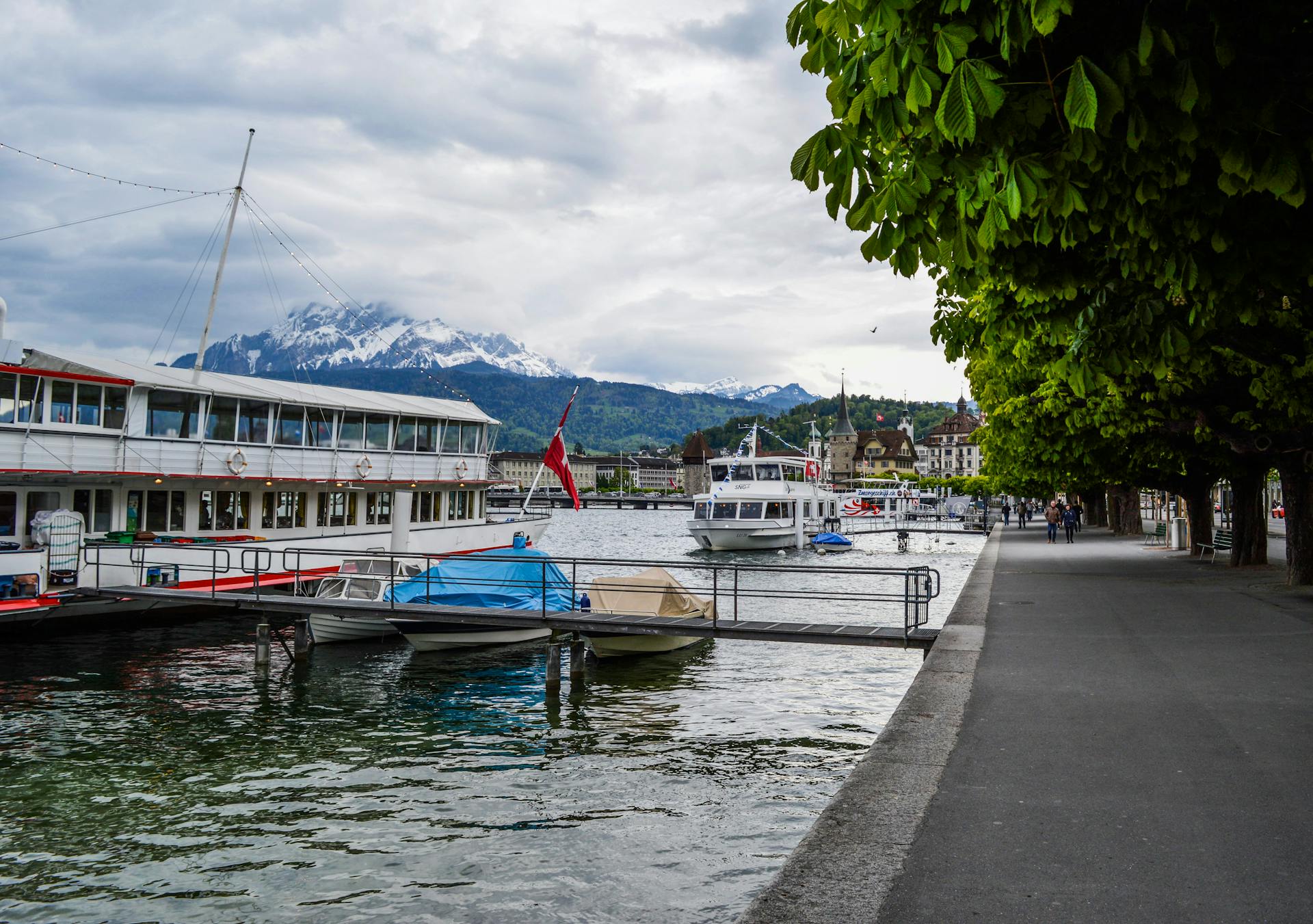 Empty paved seafront with moored boat in old town with snowy mountains in Switzerland