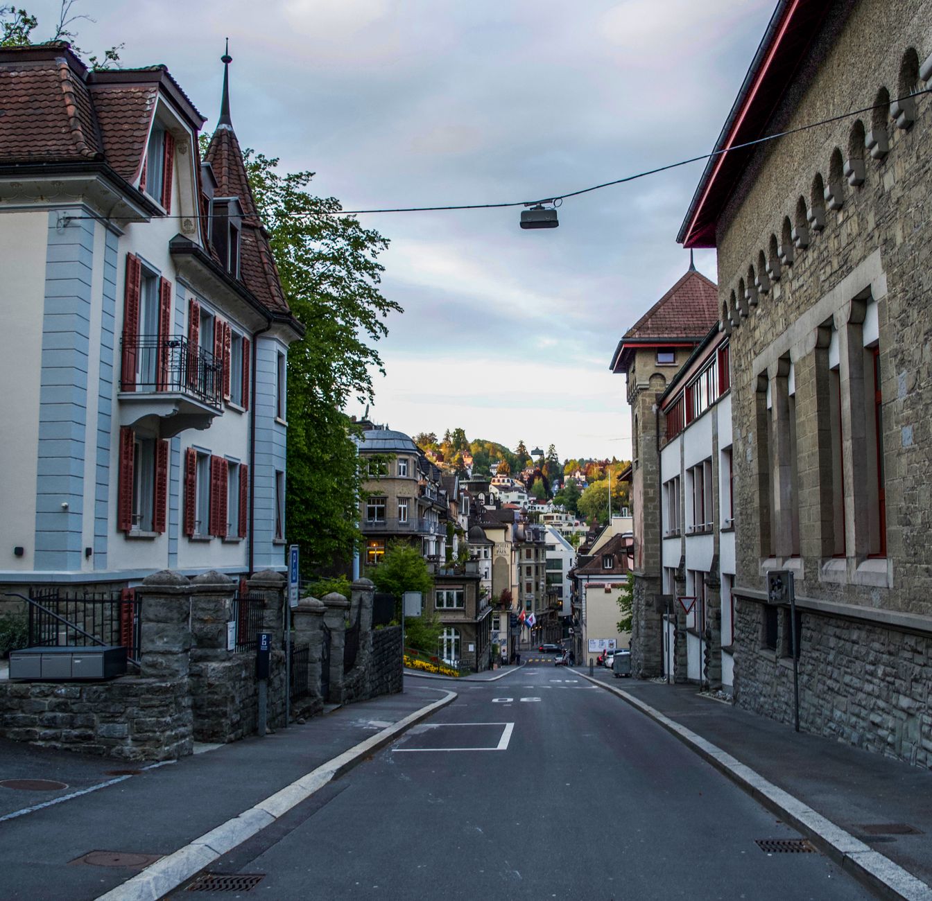 Paved street with low rise aged buildings in medieval town under cloudy sky