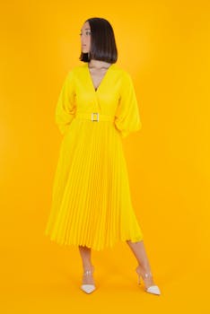 Stylish woman posing in a bright yellow dress against a matching background, exuding elegance.