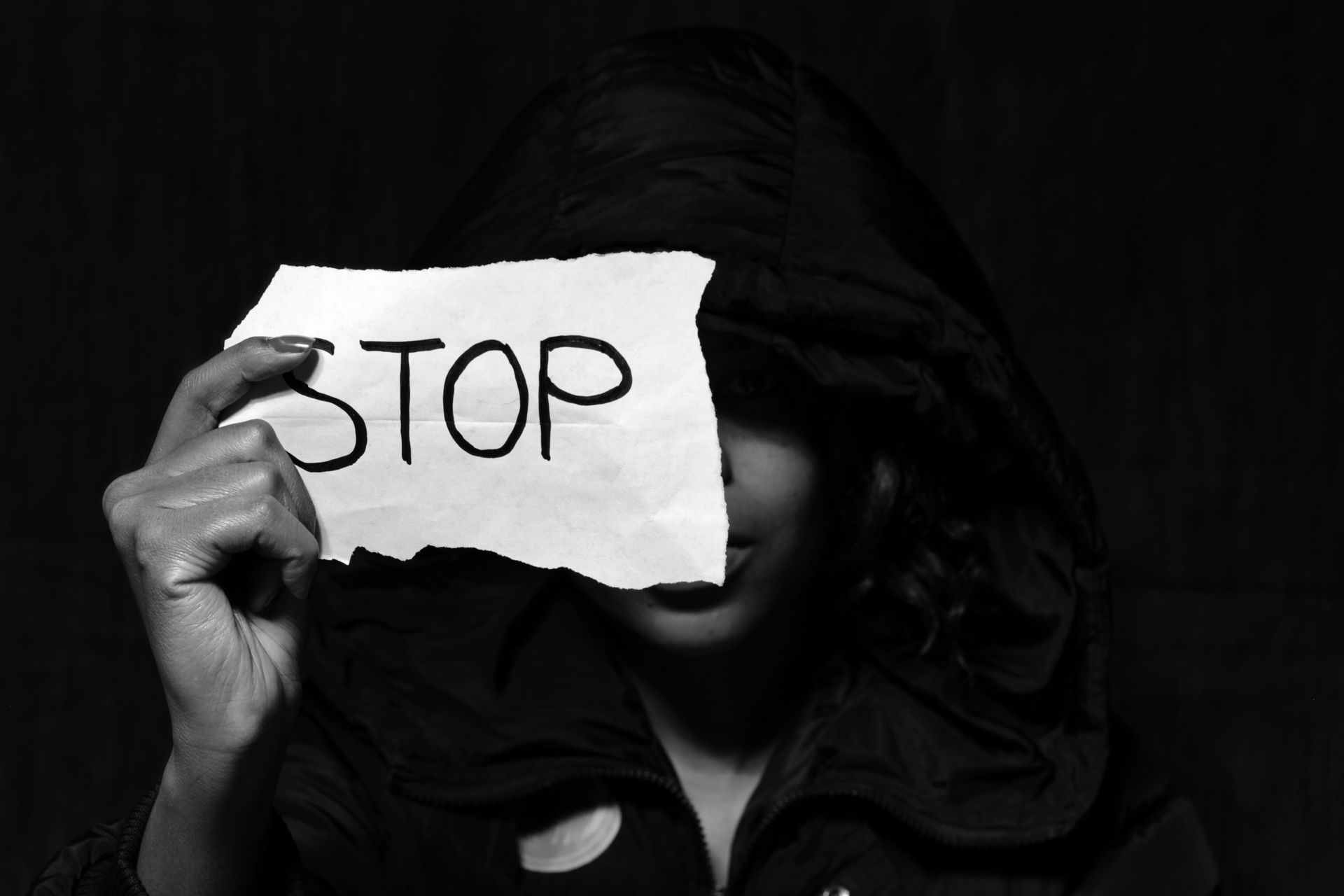 Black and white close-up of a person holding a torn paper with 'STOP' message covering face.