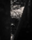 Black and white calm African American teenager with short dreadlocks standing on street and looking at camera through fence planks