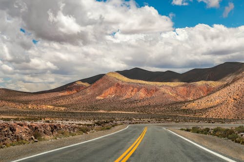 Gray Asphalt Road Near Brown Mountain Under Cloudy Sky