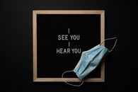 Top view of i see you i hear you inscription in simple wooden frame placed on black table near medical mask
