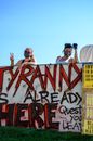 Anonymous positive young female friends in face masks standing near wall with graffiti letters and making peace sign while supporting BLM movement against blue sky