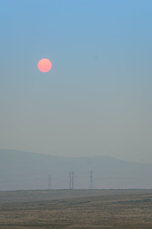 Picturesque scenery of bright sun rising over hills and fields in misty morning sky