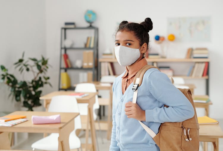 Child Wearing Facemask Standing Inside A Classroom