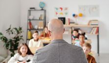 坐在办公桌前的细心学生与教室里的秃头老师互动