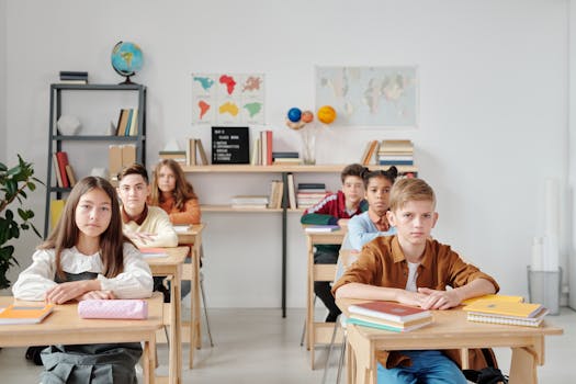 Students sit attentively in a modern classroom with books and maps, focused on learning.